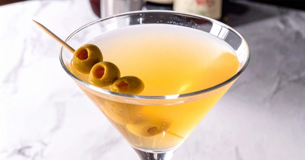 A glass of dirty martini with hot sauce, garnished with olives