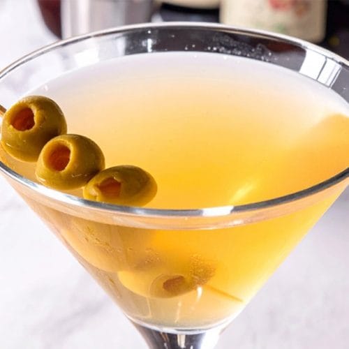 A glass of dirty martini with hot sauce, garnished with olives