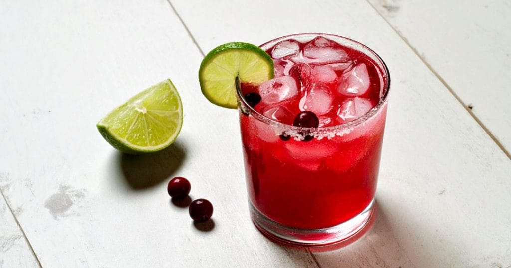Cranberry margarita garnished with fresh cranberries and lime wedge