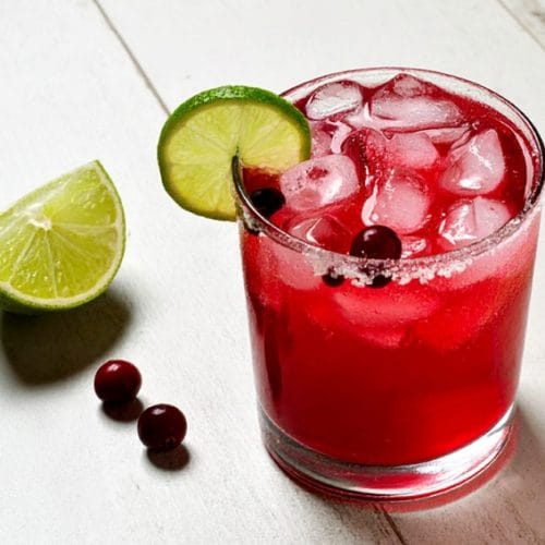 Cranberry margarita garnished with fresh cranberries and lime wedge
